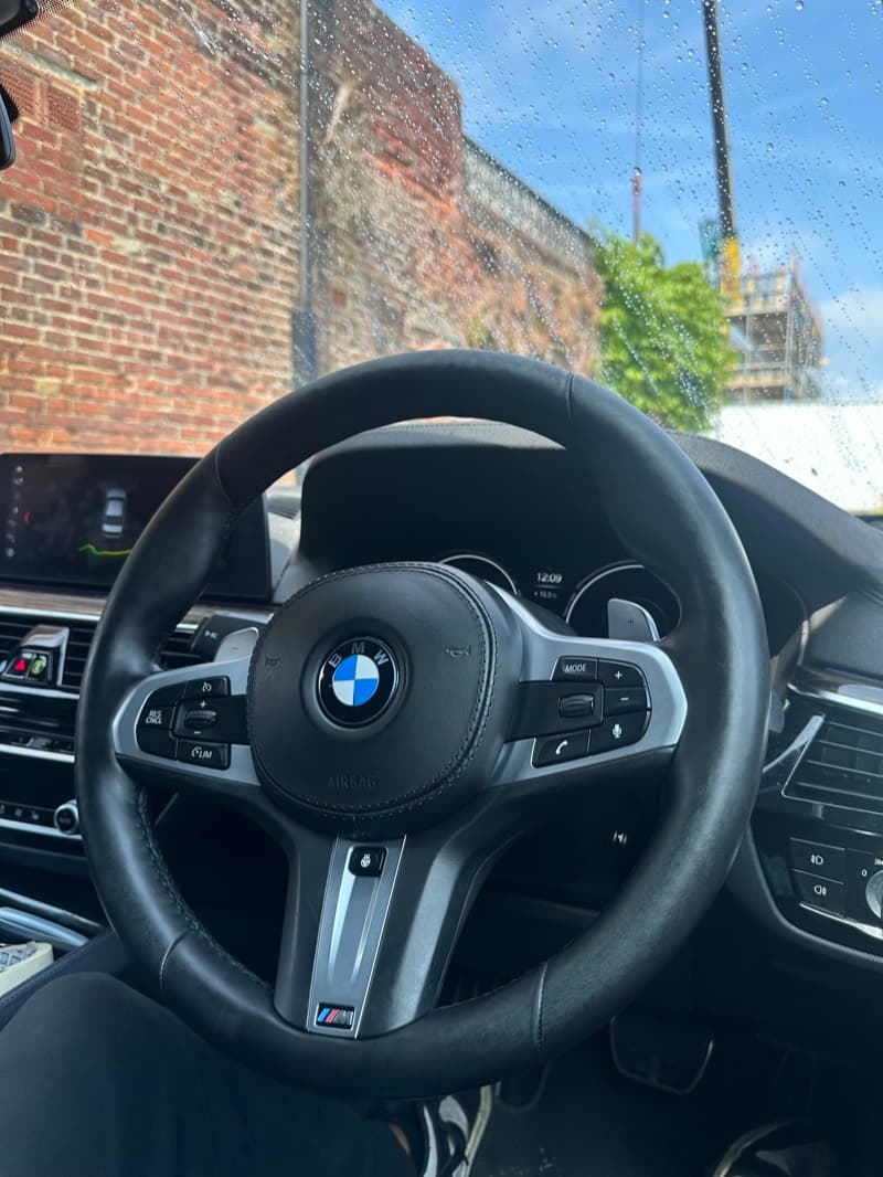 BMW steering wheel and dashboard seen through a rain-flecked windscreen